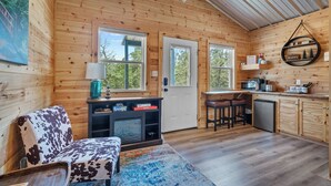 A cozy cabin interior with wooden walls, a dining area, a kitchen with a microwave, and a seating area with a cowhide-patterned chair.