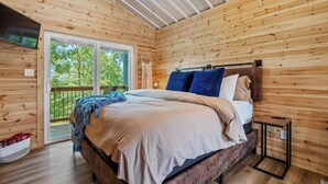 A wooden cabin bedroom with a bed, a nightstand, and a large window.