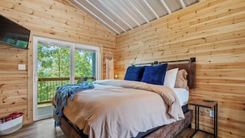 A wooden cabin bedroom with a bed, a nightstand, and a large window.