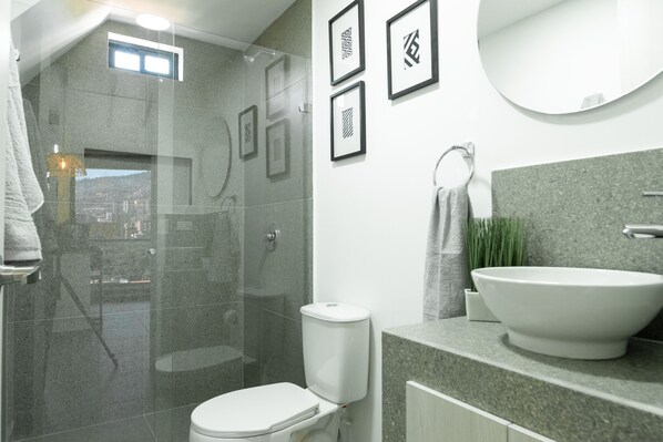 Une salle de bain moderne avec une douche à parois de verre, des toilettes blanches, un grand lavabo et des œuvres d’art encadrées accrochées au mur.