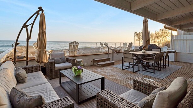 Une terrasse au bord de la plage, aménagée avec du mobilier d’extérieur et une table à manger, offrant une vue sur l’océan.
