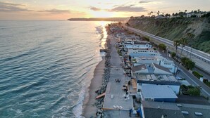 Un hôtel situé sur la côte, avec vue sur la plage, une promenade dallée et une route parallèle à la plage.