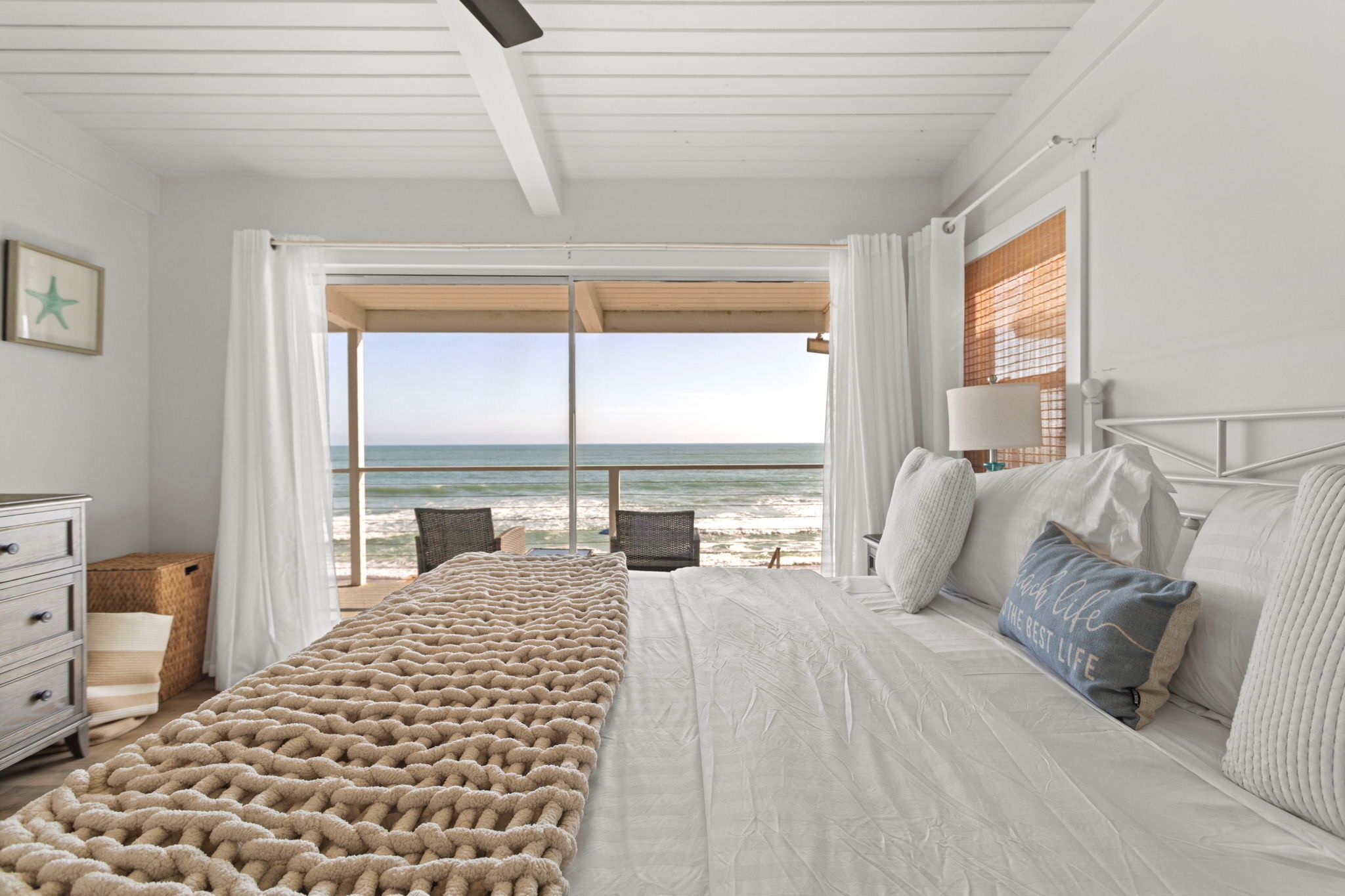 A bedroom with a large bed, a view of the beach, and a window with curtains.