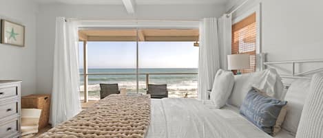 A bedroom with a large bed, a view of the beach, and a window with curtains.