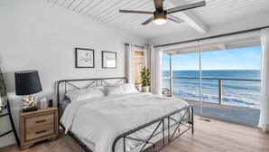 Une chambre à coucher comprenant un lit, une table de chevet, un ventilateur de plafond et une grande fenêtre donnant sur l’océan.