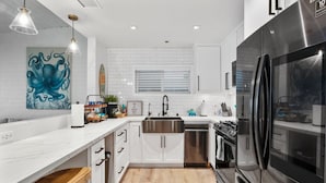 A modern kitchen with white cabinetry, a stainless steel refrigerator, and a wooden floor.