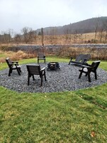 Un espacio de estar circular al aire libre con cuatro sillas Adirondack y un pozo de fuego, rodeado de grava.