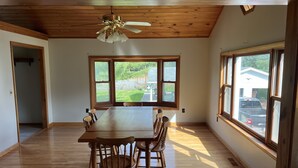Un vaste espace dédié à la salle à manger, avec une grande table et des chaises en bois, un ventilateur de plafond et de grandes fenêtres offrant une vue sur l’extérieur.