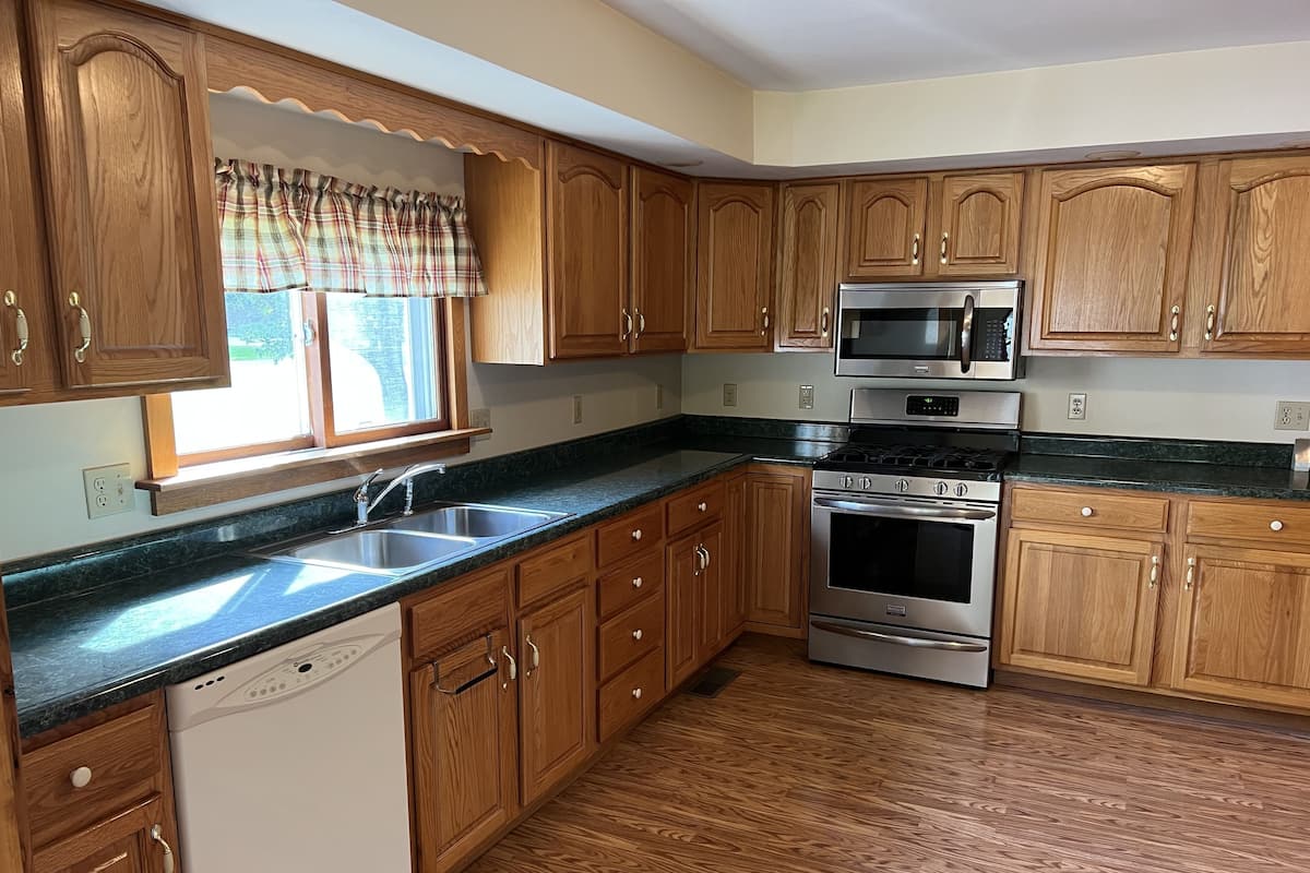 Una cocina con gabinetes de madera, estufa de acero inoxidable, microondas y lavavajillas.