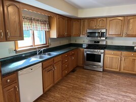 Una cocina con gabinetes de madera, estufa de acero inoxidable, microondas y lavavajillas.