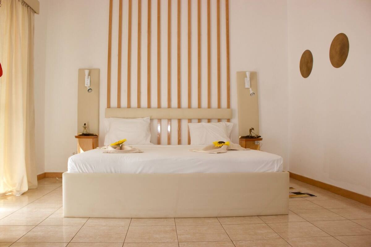 Ein großes Bett mit Holz-Kopfstück, zwei Nachttische mit Lampen und eine Wand mit vertikalen Holzleisten.