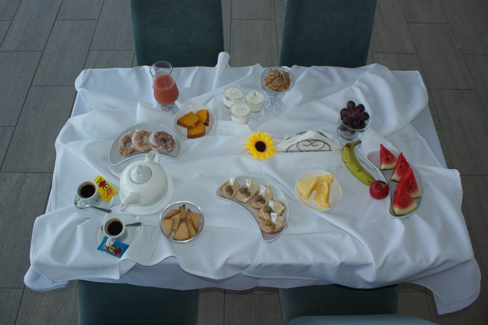 A table set with various breakfast items including pastries, fruits, and beverages, arranged on a white tablecloth.