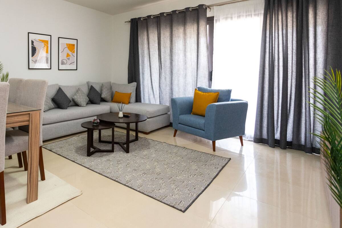 A modern living room with a grey sofa, blue armchair, and a dining table with chairs.