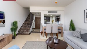 Een moderne woonkamer met een bank, salontafel en een eethoek. Een trap leidt naar een keuken en eetkamer.