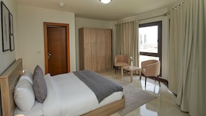 Een slaapkamer met een bed, een kledingkast, een stoel, een klein tafeltje en een raam met gordijnen.