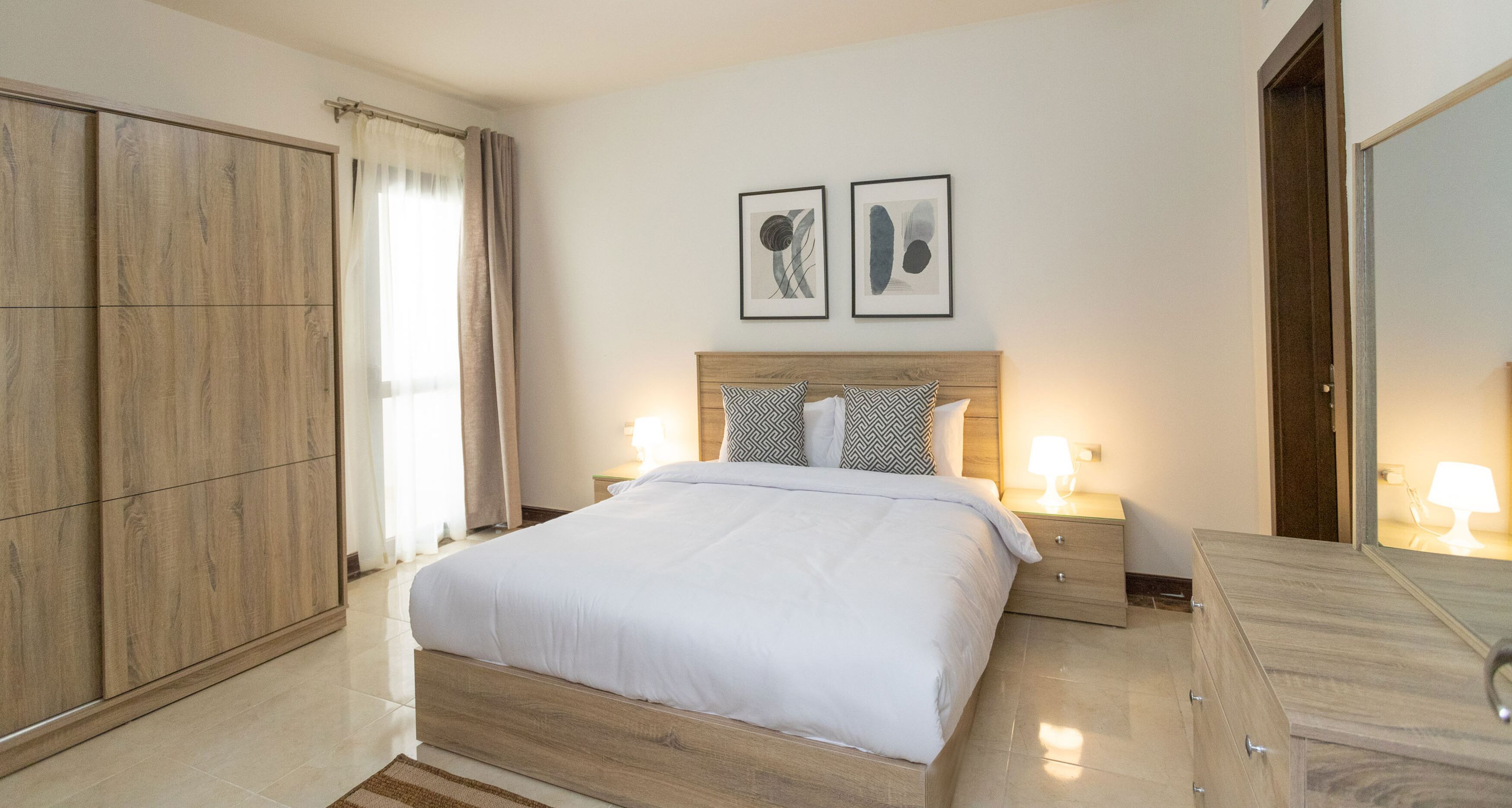 Ein Hotelzimmer mit einem großen Bett, zwei Nachttischen mit Lampen, einem Kleiderschrank und zwei gerahmten Bildern an der Wand.