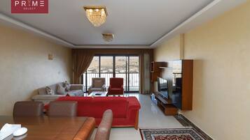 Un salón amplio con un sofá rojo, una mesa de comedor de madera y un televisor sobre un mueble de madera.