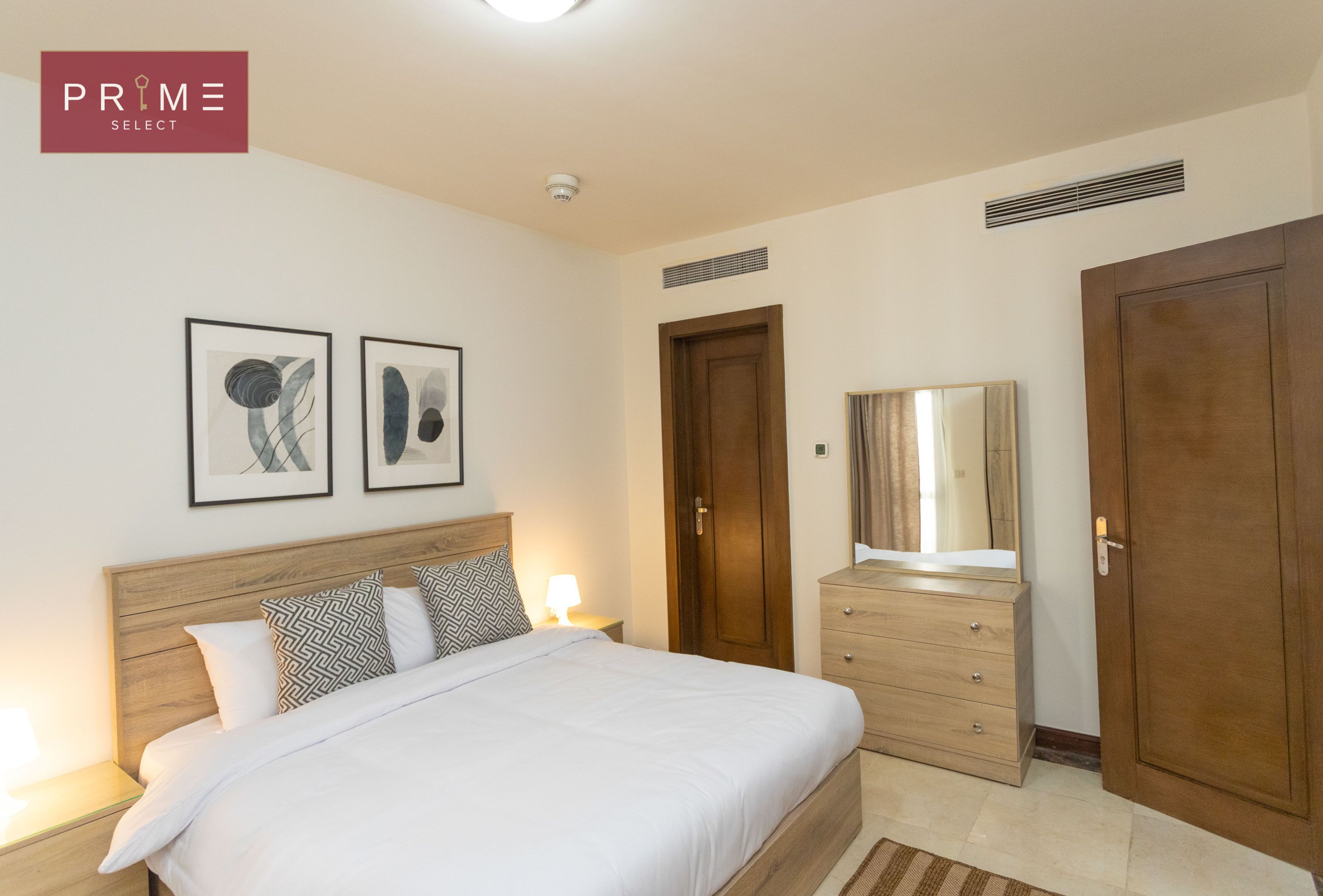A hotel room with a bed, a dresser, a mirror, and two framed artworks on the wall.