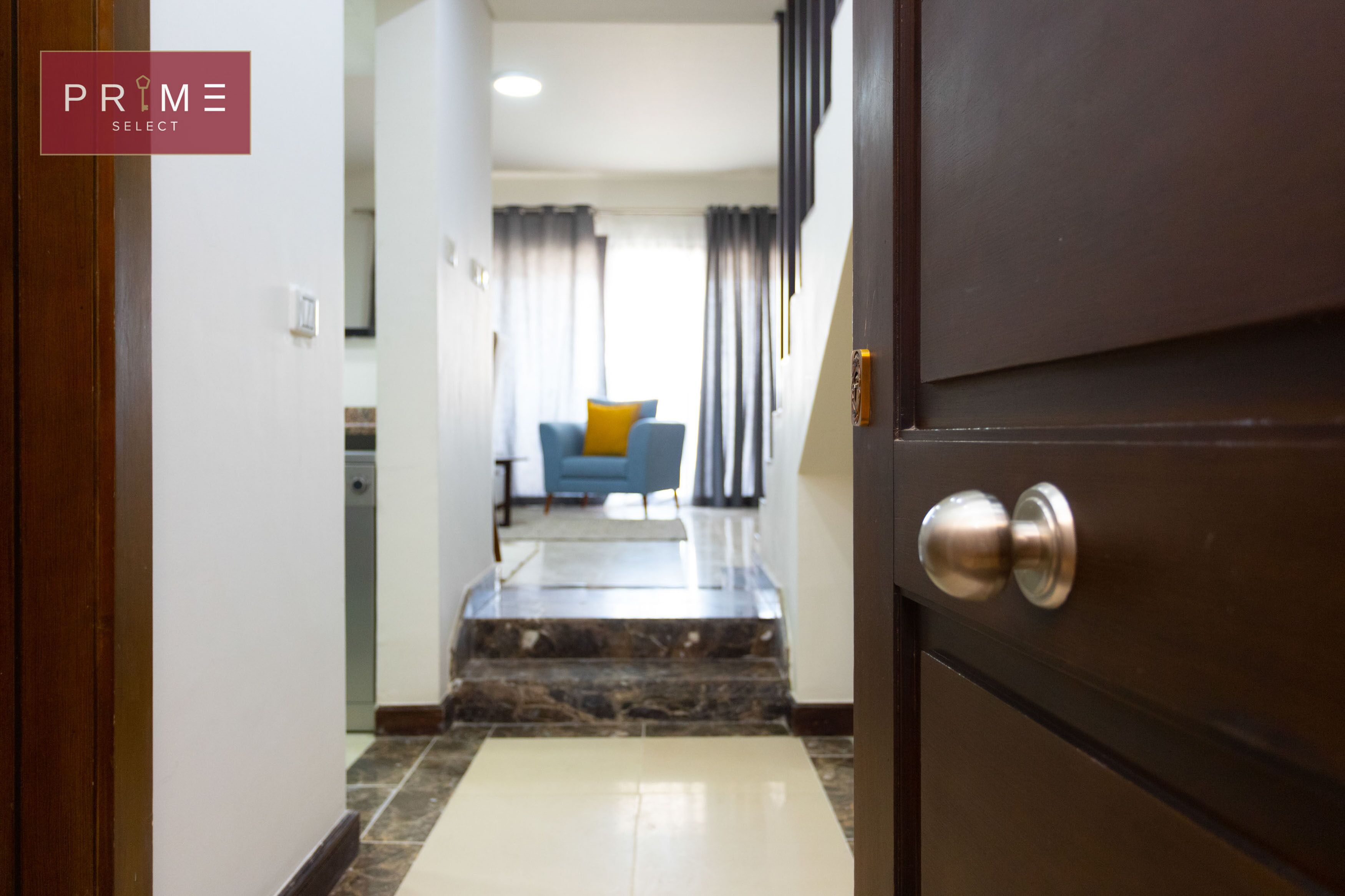 A hotel entrance with a marble floor, a wooden door, and a view into a living area with a sofa and curtains.