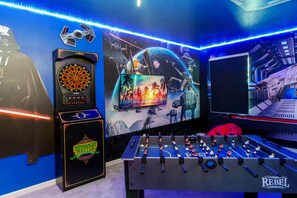 Una habitación con dardos, mesa de futbolín, una pantalla grande y decoración temática de Star Wars.