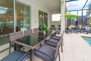 A glass-enclosed patio with a dining table, chairs, and a potted plant.