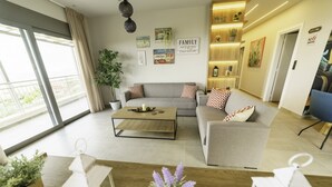 A modern living room with a sofa, coffee table, and decorative pillows. There are wall art pieces and a sign that reads "WELCOME". - Royal Hill Villa (Hersonissos)