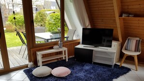 Una habitación acogedora con un televisor grande, muebles de madera y vistas al jardín.