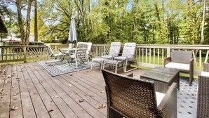 A wooden deck with wicker furniture, including chairs and a table, surrounded by trees.