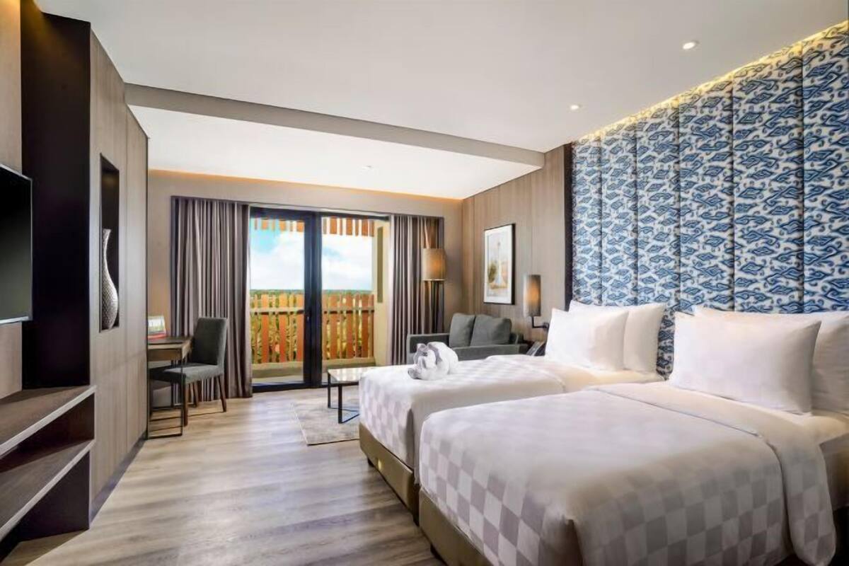 Habitación de hotel con dos camas, un escritorio, una silla, un televisor y vistas al exterior.