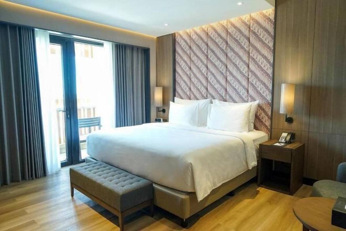 Habitación de hotel con una cama grande, una banca, una mesita de noche con un teléfono y vistas al exterior.