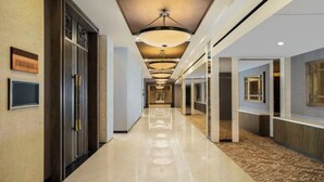 Un corridoio d'hotel con pavimento lucido, un lampadario al centro e un cartello appeso al muro.
