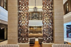 A lobby with a central decorative panel, seating area, and a chandelier. - Swiss-Belhotel Airport Yogyakarta (Temon)