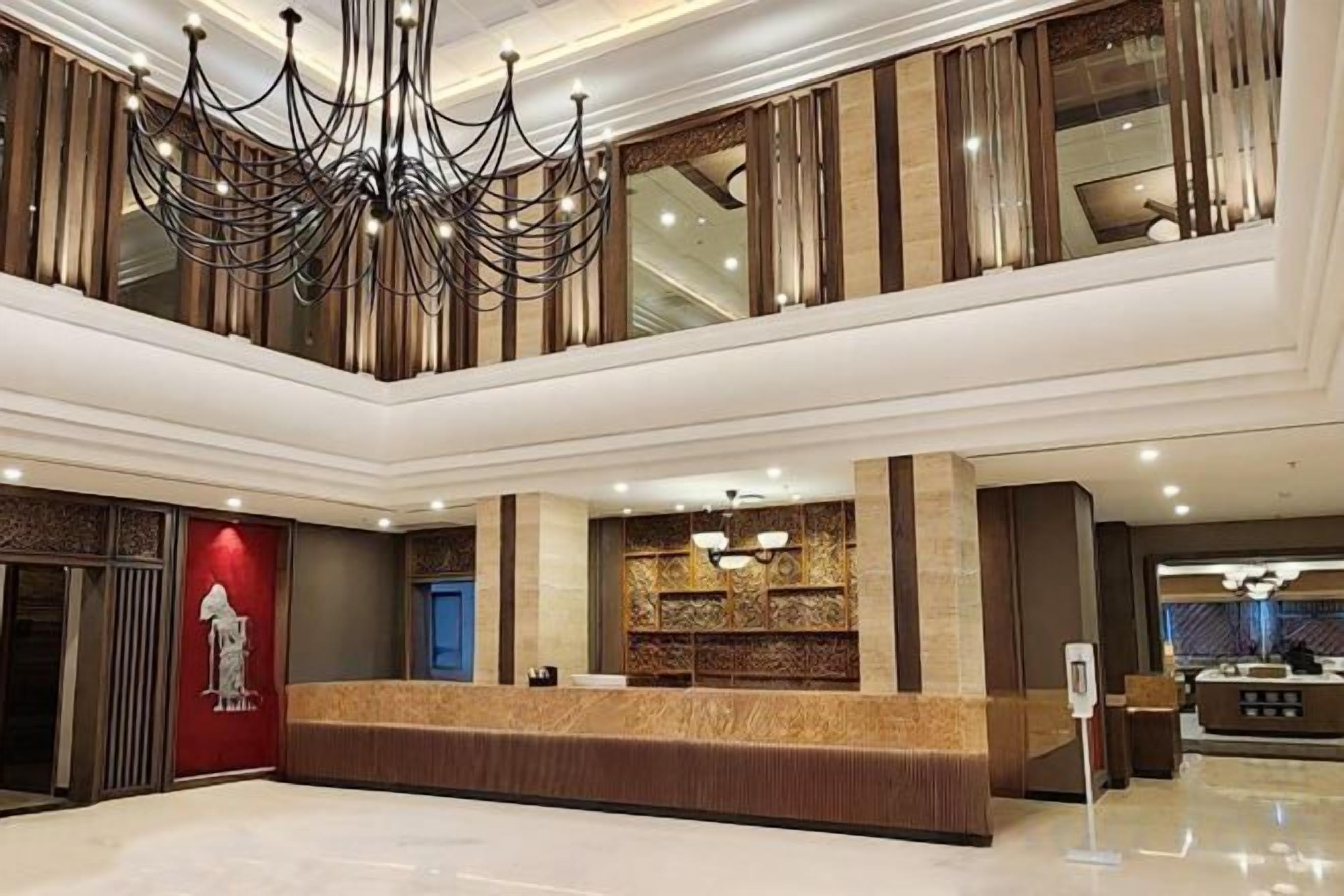 A hotel lobby with a reception desk, a chandelier, and a seating area.