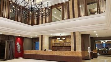 A hotel lobby with a reception desk, a chandelier, and a seating area.