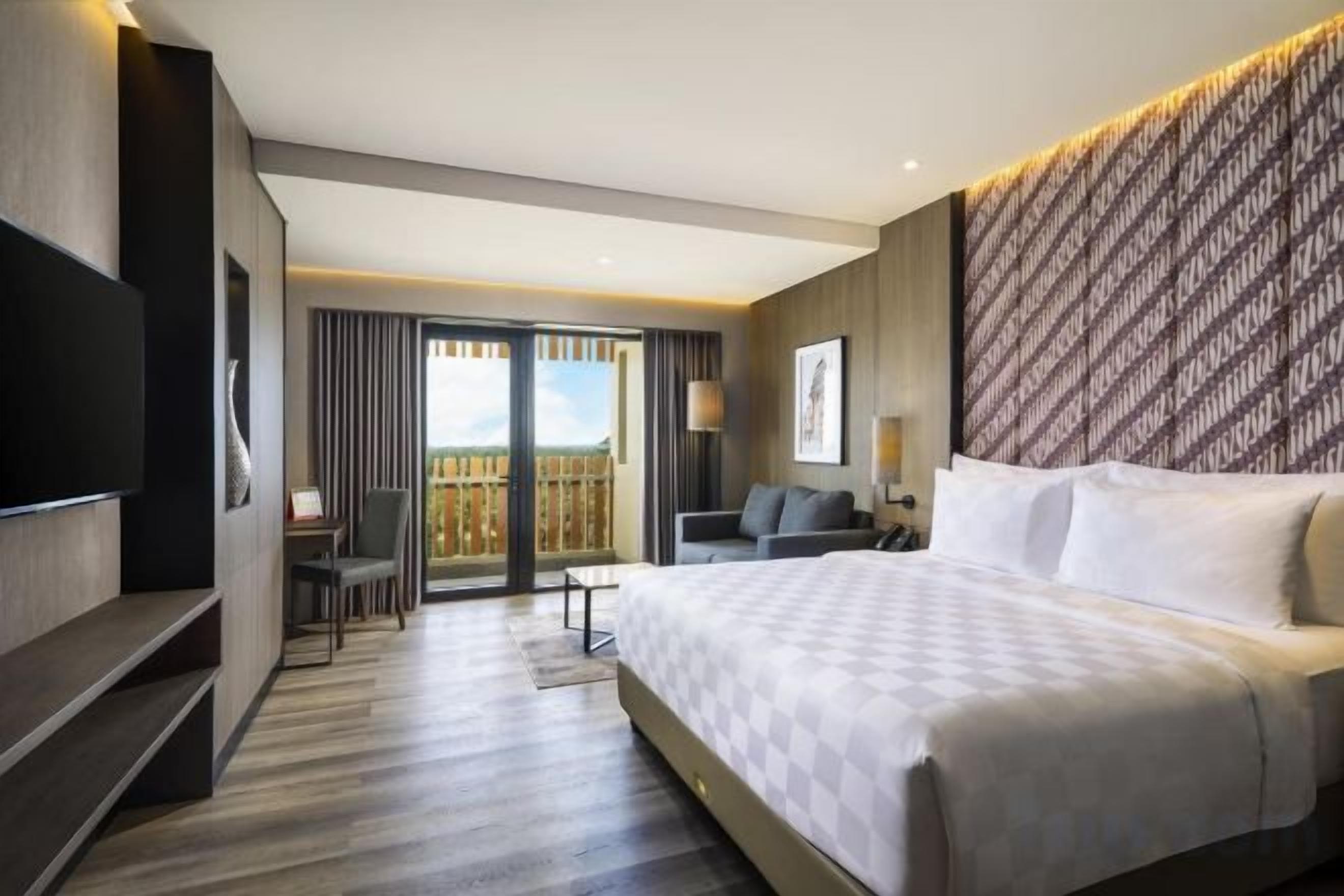 Una habitación de hotel con una cama grande, televisor, escritorio y balcón con vistas.