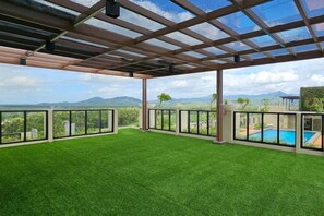 An outdoor patio with artificial grass, a pool, and a view of mountains. - Swiss-Belhotel Airport Yogyakarta (Temon)