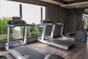 A gym with treadmills and exercise bikes, large windows, and a view of greenery. - Swiss-Belhotel Airport Yogyakarta (Temon)
