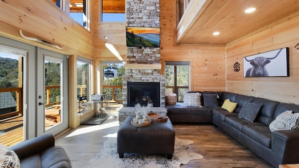 Un salón amplio con chimenea de piedra, un sofá grande y vistas al exterior.