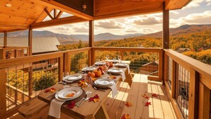 Terraza de madera con una mesa lista para comer, con vistas a un paisaje montañoso.