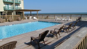 A pool area with wooden deck chairs and a view of the ocean. - Beachfront Two Bedroom Condo with a Pool/2 nights or 7 nights. Pet friendly! (Freeport)