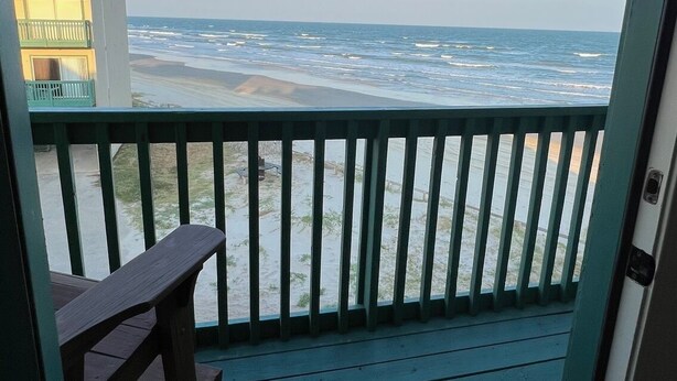 A balcony with a view of the ocean, a wooden bench, and a building in the background. - Beachfront Two Bedroom Condo with a Pool/2 nights or 7 nights. Pet friendly! (Freeport)
