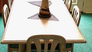 A dining table with chairs, a decorative lighthouse centerpiece, and a view of a green deck through a door. - Beachfront Two Bedroom Condo with a Pool/2 nights or 7 nights. Pet friendly! (Freeport)