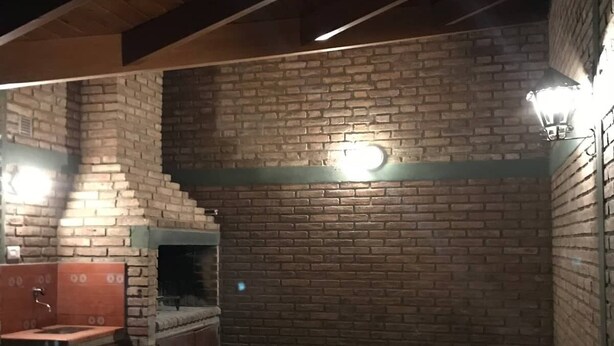 Una cocina exterior de ladrillo con pileta y alacenas, bajo un techo inclinado con vigas de madera a la vista.
