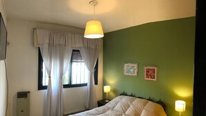 Un dormitorio con cama, dos lámparas de noche, una ventana con cortinas y dos obras de arte en la pared.