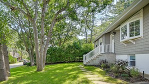 A residential property with a well-maintained lawn, a stone pathway leading to the front door, and mature trees providing shade. - Hampton Bays Retreat: Walk to Squires Beach! (Hampton Bays)