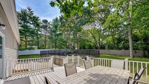 A wooden deck with a table and chairs, surrounded by a white fence and trees. - Hampton Bays Retreat: Walk to Squires Beach! (Hampton Bays)