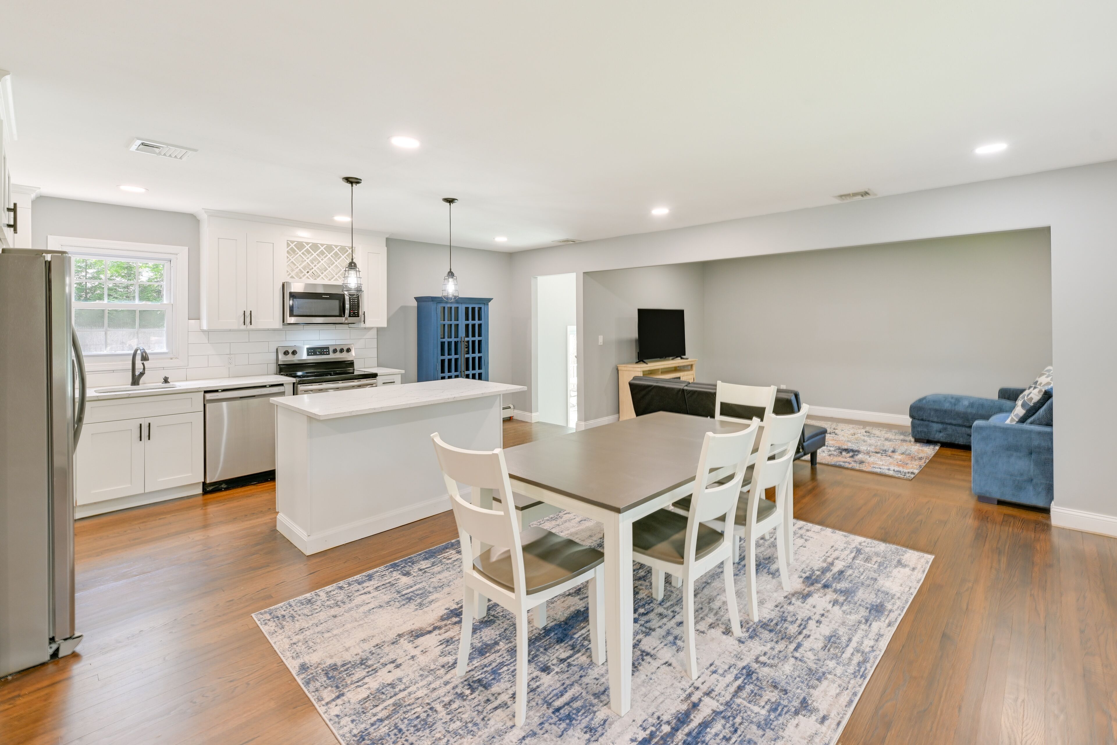 A modern kitchen with white cabinetry, a central island, and a dining area with a table and chairs.