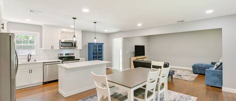A modern kitchen with white cabinetry, a central island, and a dining area with a table and chairs.