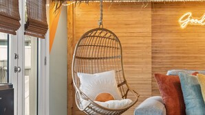 Una habitación con una silla colgante, un sofá con cojines de colores y un letrero de neón en la pared.