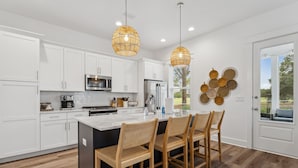 Una cocina moderna con armarios blancos, una isla grande y sillas de madera.